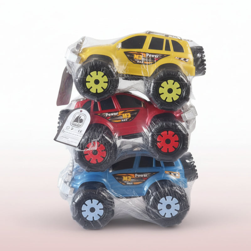 Three toy monster trucks in packaging on a wooden surface with a beige wall background.