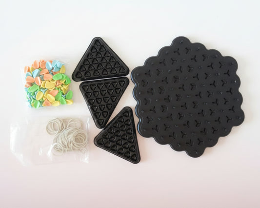 Black silicone mats with star and triangle patterns, and small bags of colorful beads and clear rubber bands on a wooden surface.