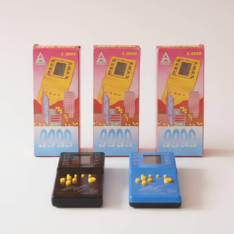 Two handheld electronic games, one black and one blue, with their packaging in the background.