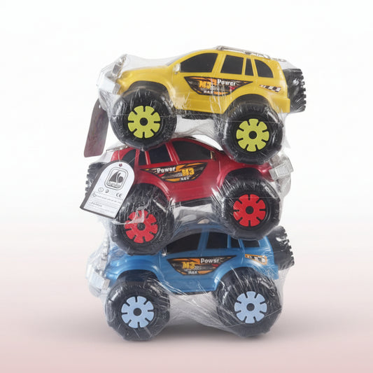 Three toy monster trucks in packaging on a wooden surface with a beige wall background.