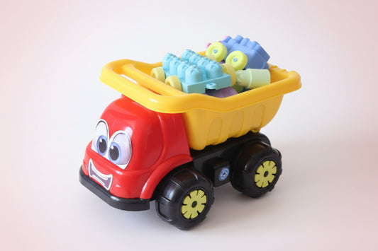 Red toy truck with yellow bed containing colorful building blocks on a wooden surface.
