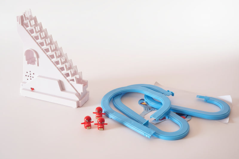 Toy track set with a white staircase-like structure, blue tracks, and red cars on a wooden surface.
