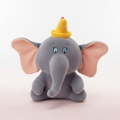 Plush elephant toy with a yellow hat on a wooden surface