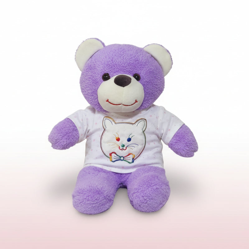 Purple teddy bear wearing a white shirt with a cat design on a wooden surface.