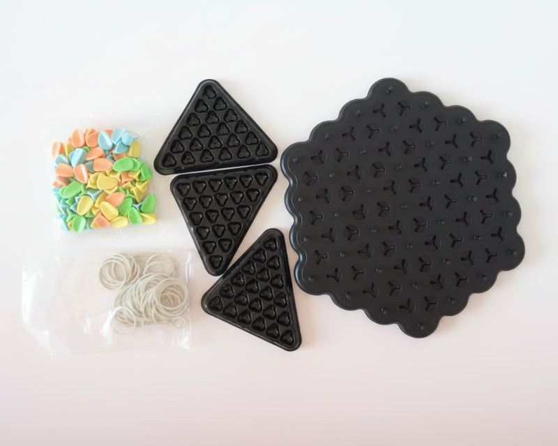 Black silicone mats with star and triangle patterns, and small bags of colorful beads and clear rubber bands on a wooden surface.