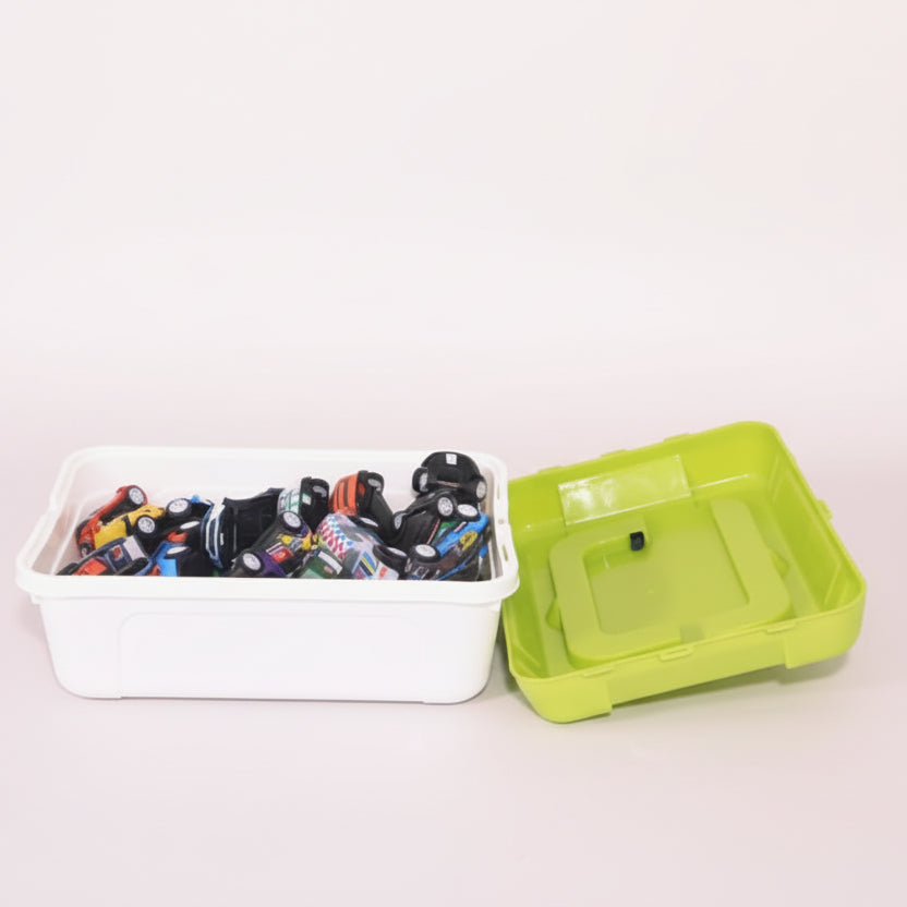 White storage bin with toy cars next to a green lid on a wooden surface