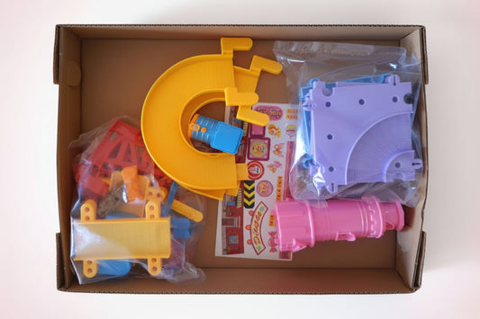 Toy building set with various pieces in a cardboard box on a wooden surface