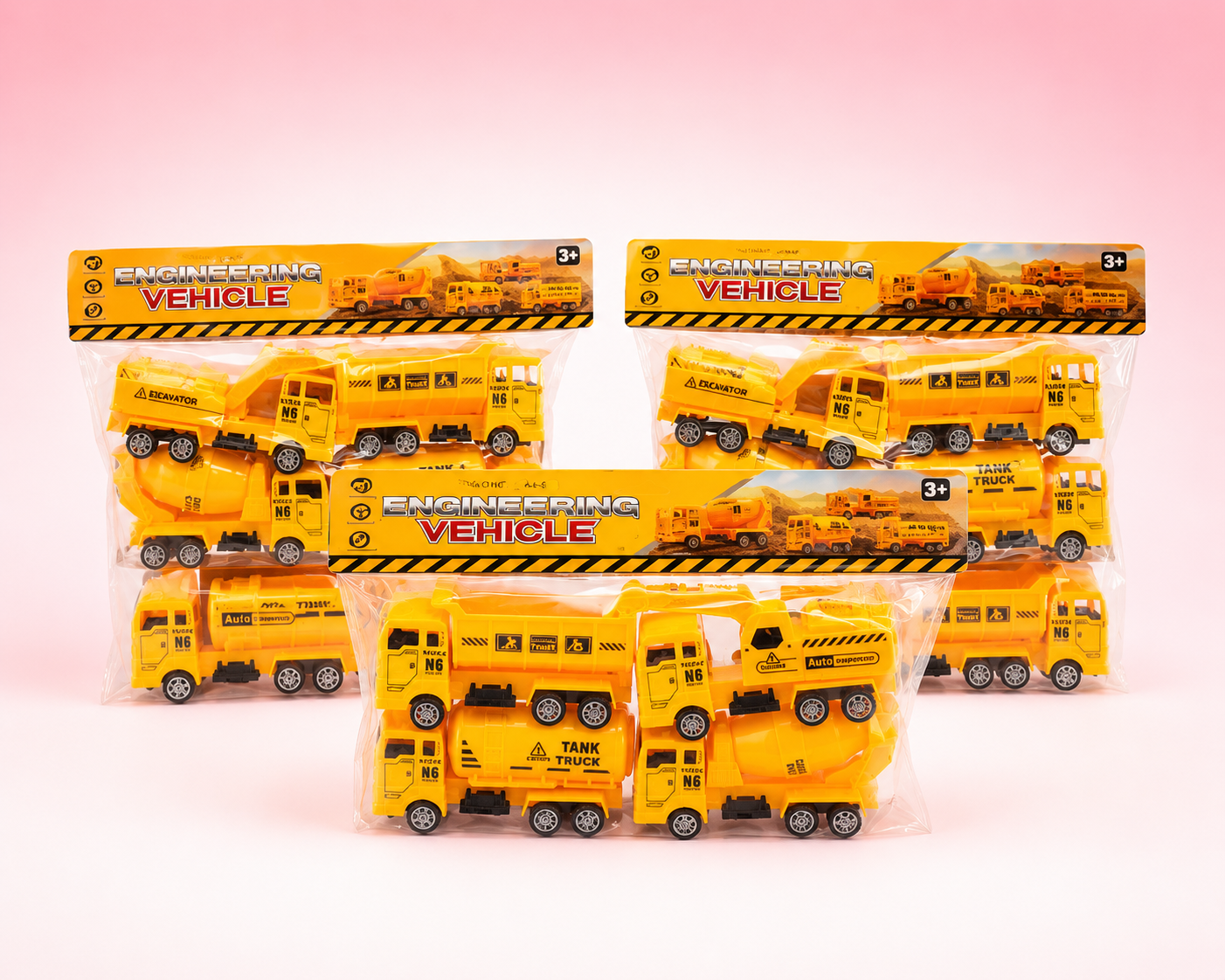 Five packaged yellow toy construction vehicles, including dump trucks and a cement mixer, arranged on a soft pink studio background. Each toy is sealed in clear plastic with a printed header card reading "ENGINEERING VEHICLE.