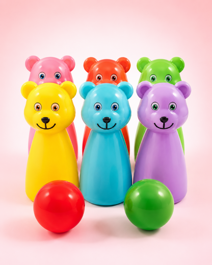 A set of colorful bear-shaped toy bowling pins and balls on a soft pink studio background. The front row shows a red ball in front of a yellow bear, a green ball in front of a purple bear, with blue, pink, orange, and green bear pins standing behind them.