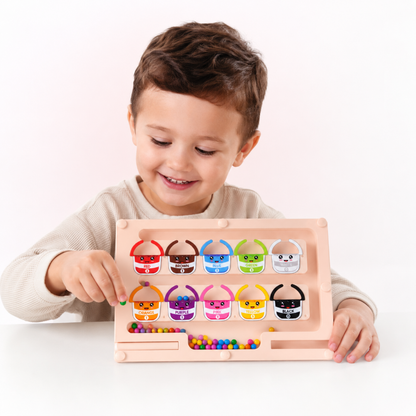 A young child smiling and playing with a pastel pink wooden bead sorting toy on a clean white background.