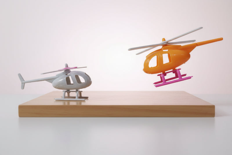 Two toy helicopters, one white and one orange with pink accents, on a wooden surface.