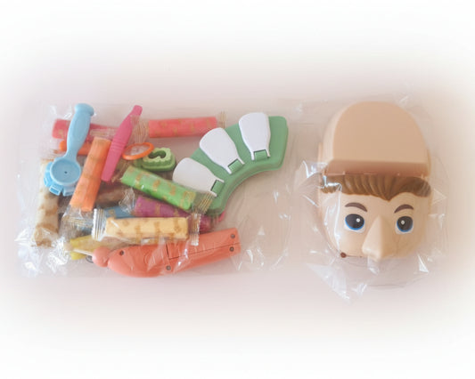 Toy figure parts including a head and various accessories on a wooden surface.