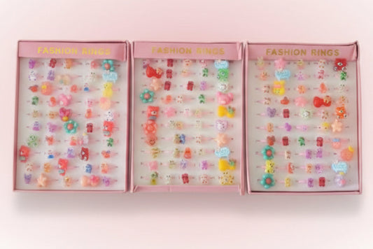 Three pink boxes filled with colorful fashion rings on a wooden surface.