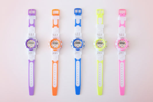 Five colorful digital watches with different colored straps on a wooden surface.