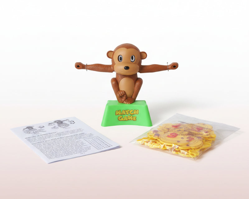 Toy monkey on a stand with a 'Match Game' label, plastic bag with yellow shapes, and paper instructions on a wooden surface.