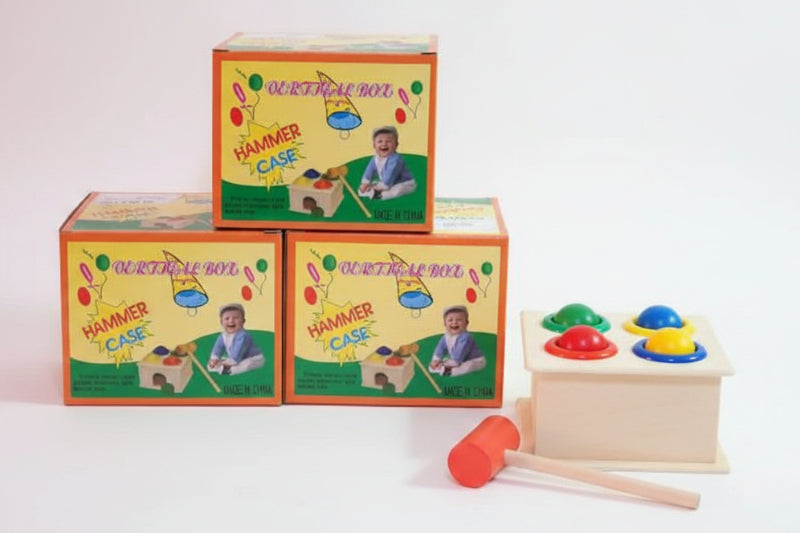 Children's educational toy with colorful boxes labeled 'Hammer and Ball' on a wooden surface.