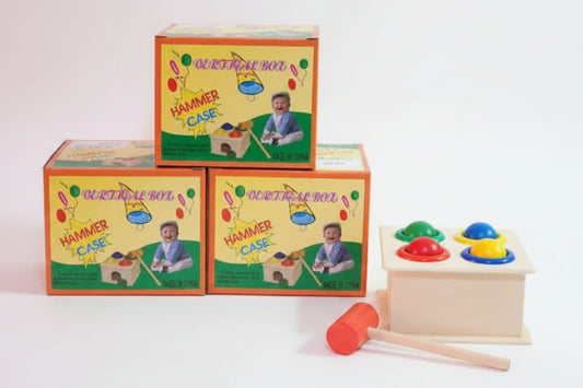 Children's educational toy with colorful boxes labeled 'Hammer and Ball' on a wooden surface.